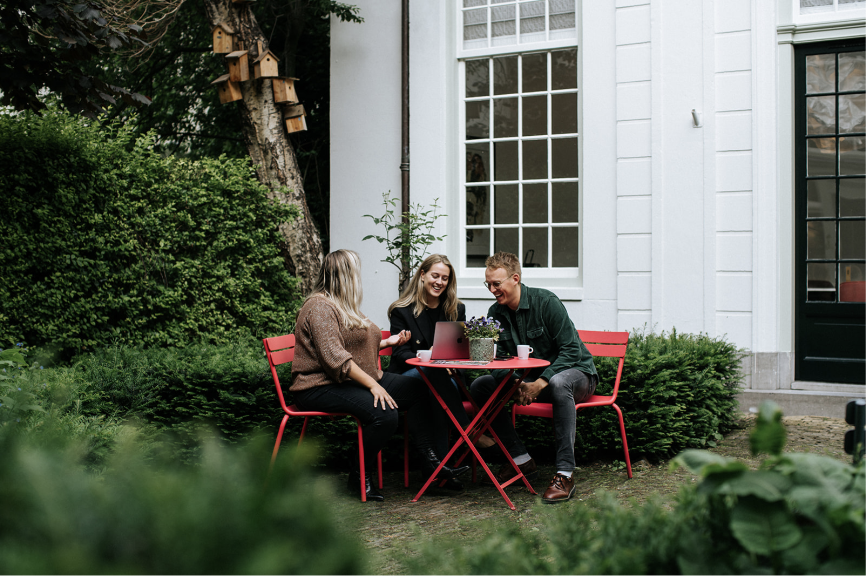 Drie professionals vergaderen buiten in de rustige binnentuin van EBC Amsterdam aan de Herengracht.