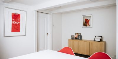 Moderne vergaderruimte 'Ajax' bij EBC Amsterdam met een gesigneerd voetbalshirt aan de wand en rode designstoelen.