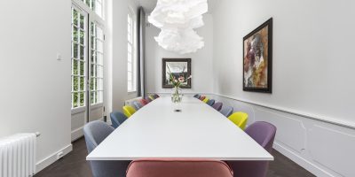 Moderne vergaderruimte in het tuinhuis van EBC Amsterdam met een lange witte tafel, kleurrijke designstoelen en veel daglicht.